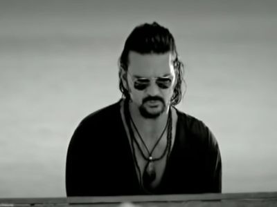 Ricardo Arjona is playing a piano in the beach.